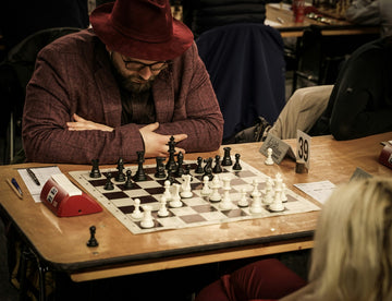 man sitting before standard chess board, chess clock, and opponent