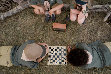 A group of four people surround a chessboard placed in the grass.